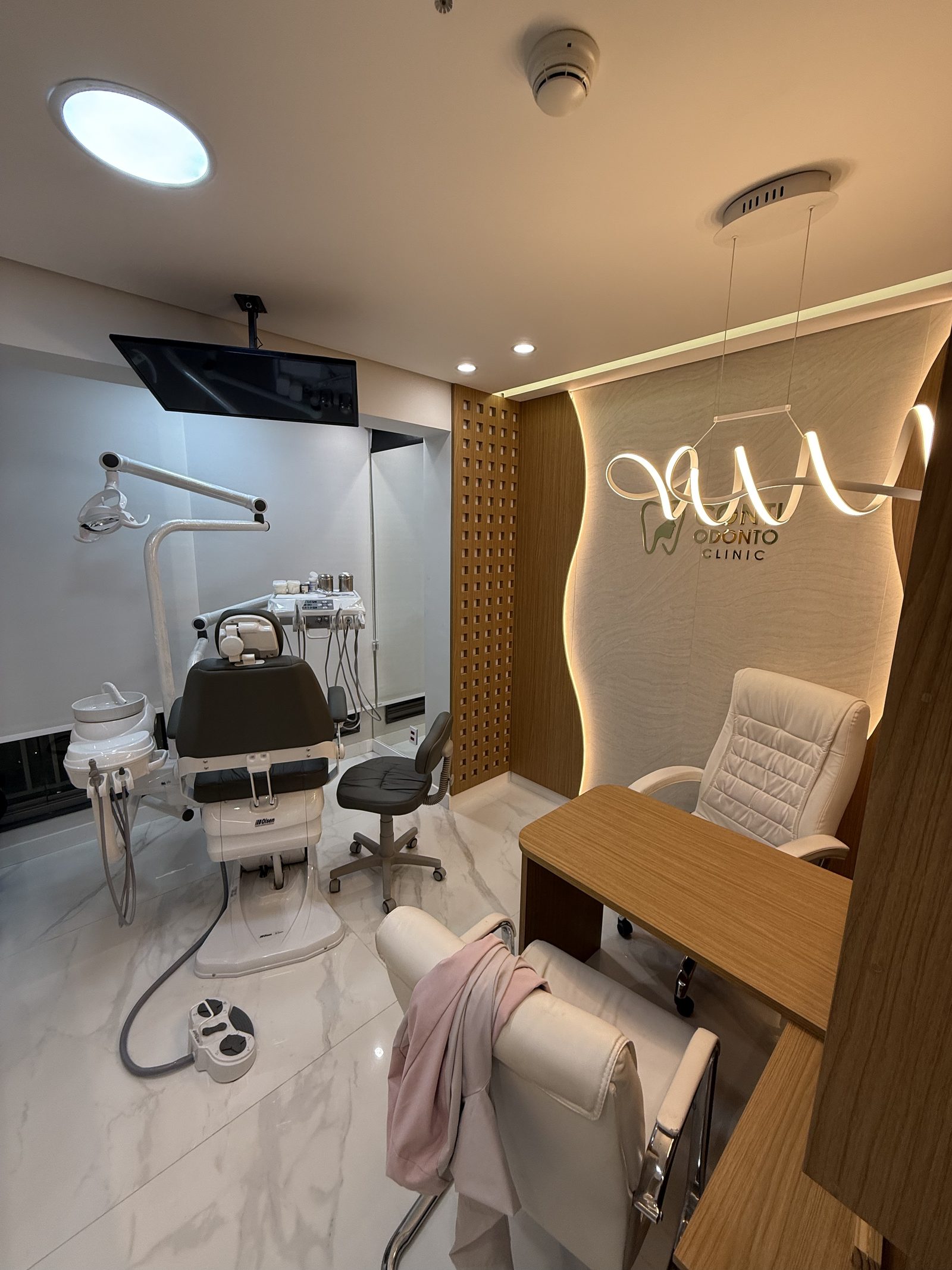 Cadeira odontológica diante de painel de madeira ondulado com logotipo iluminado